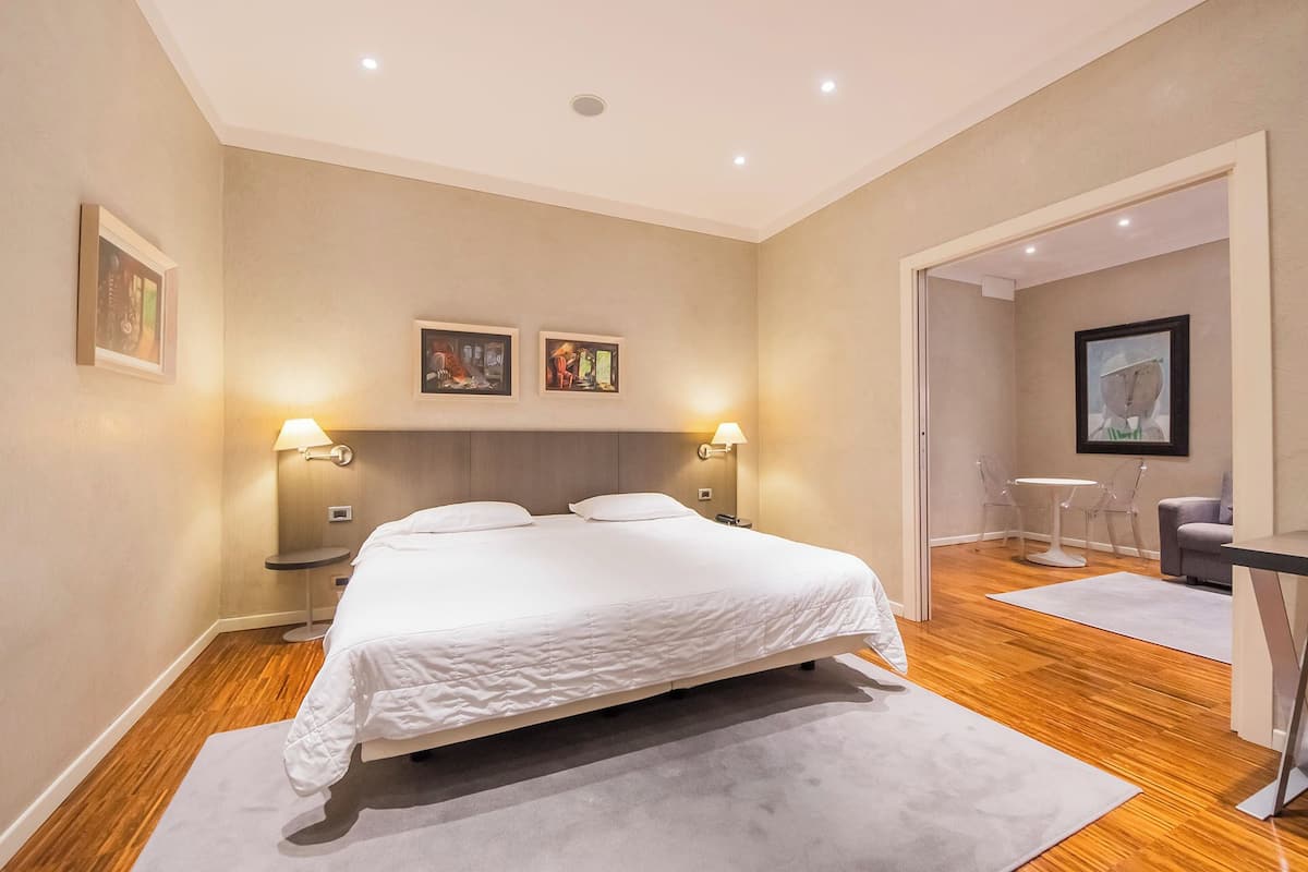 A modern hotel room with a large bed, two bedside lamps, and artwork on the walls.