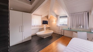 A modern bedroom with a skylight, a large bathtub, a bed, and a desk area. - Century Hotel (Parma)