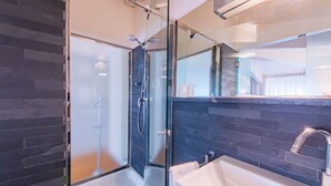 A modern bathroom with a glass-enclosed shower, a white sink, and dark tiled walls. - Century Hotel (Parma)