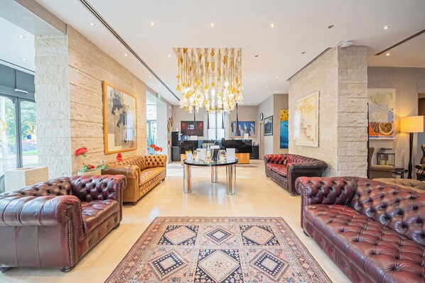 A spacious lobby with leather sofas, a central coffee table, and a chandelier. - Century Hotel (Parma)
