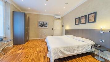 Quarto de hotel com uma cama grande, piso de madeira, escrivaninha com cadeira, guarda-roupa e um quadro na parede.