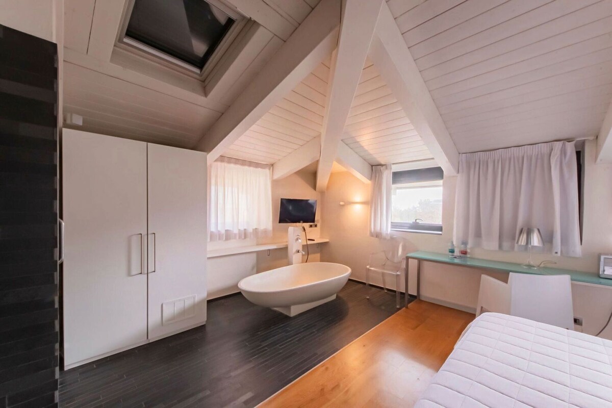 Un dormitorio moderno con una cama grande, una bañera integrada, un escritorio y un televisor.
