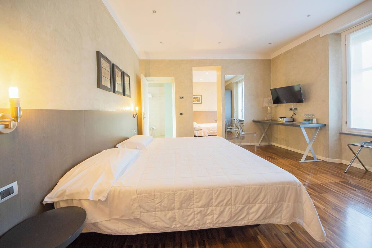A hotel room with a large bed, a desk with a TV, and a chair.