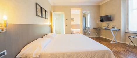 A hotel room with a large bed, a desk with a TV, and a chair.