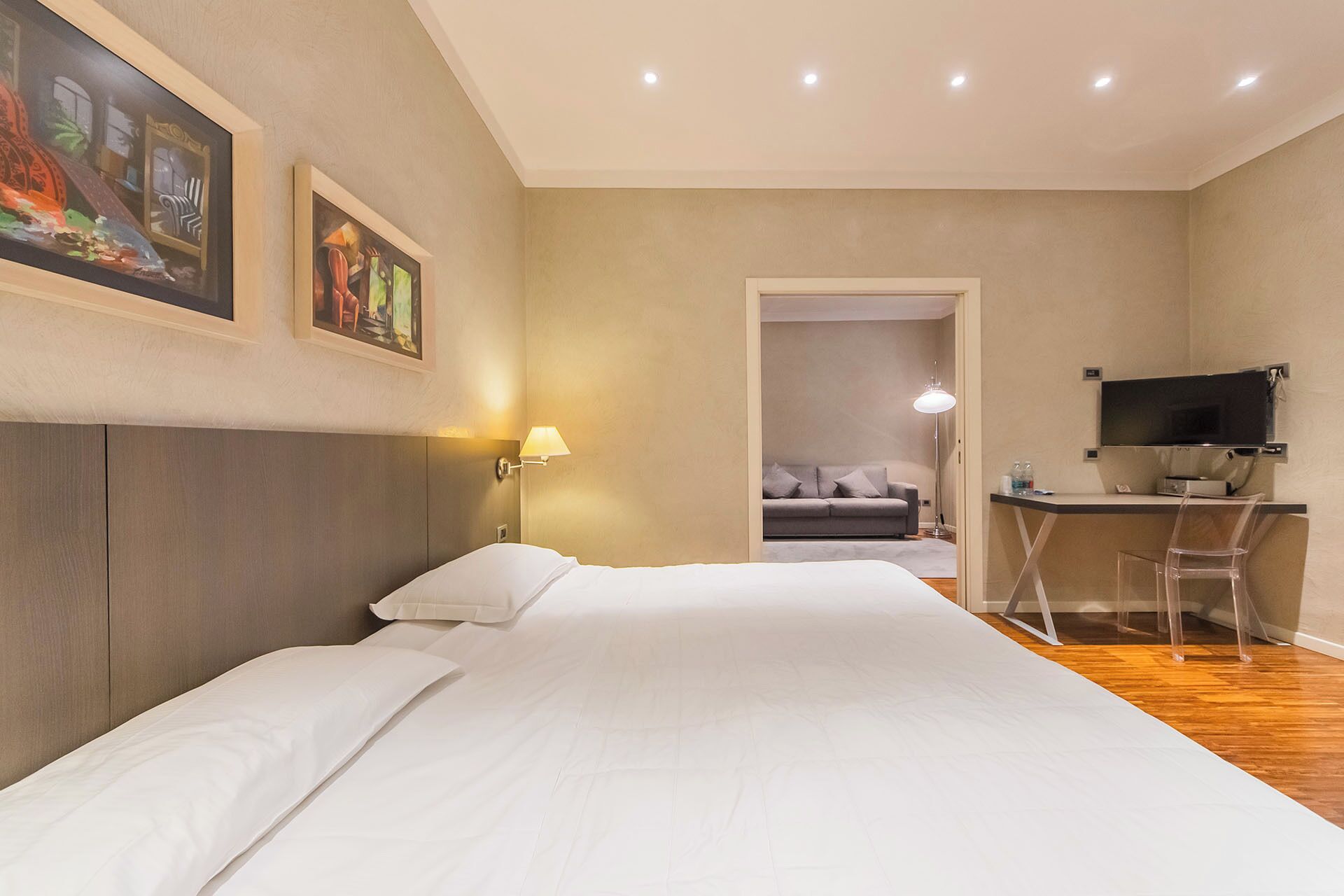 A hotel room with a bed, a desk, a chair, a TV, and artwork on the walls.