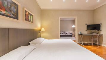 A hotel room with a bed, a desk, a chair, a TV, and artwork on the walls.
