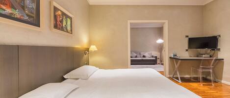 A hotel room with a bed, a desk, a chair, a TV, and artwork on the walls.
