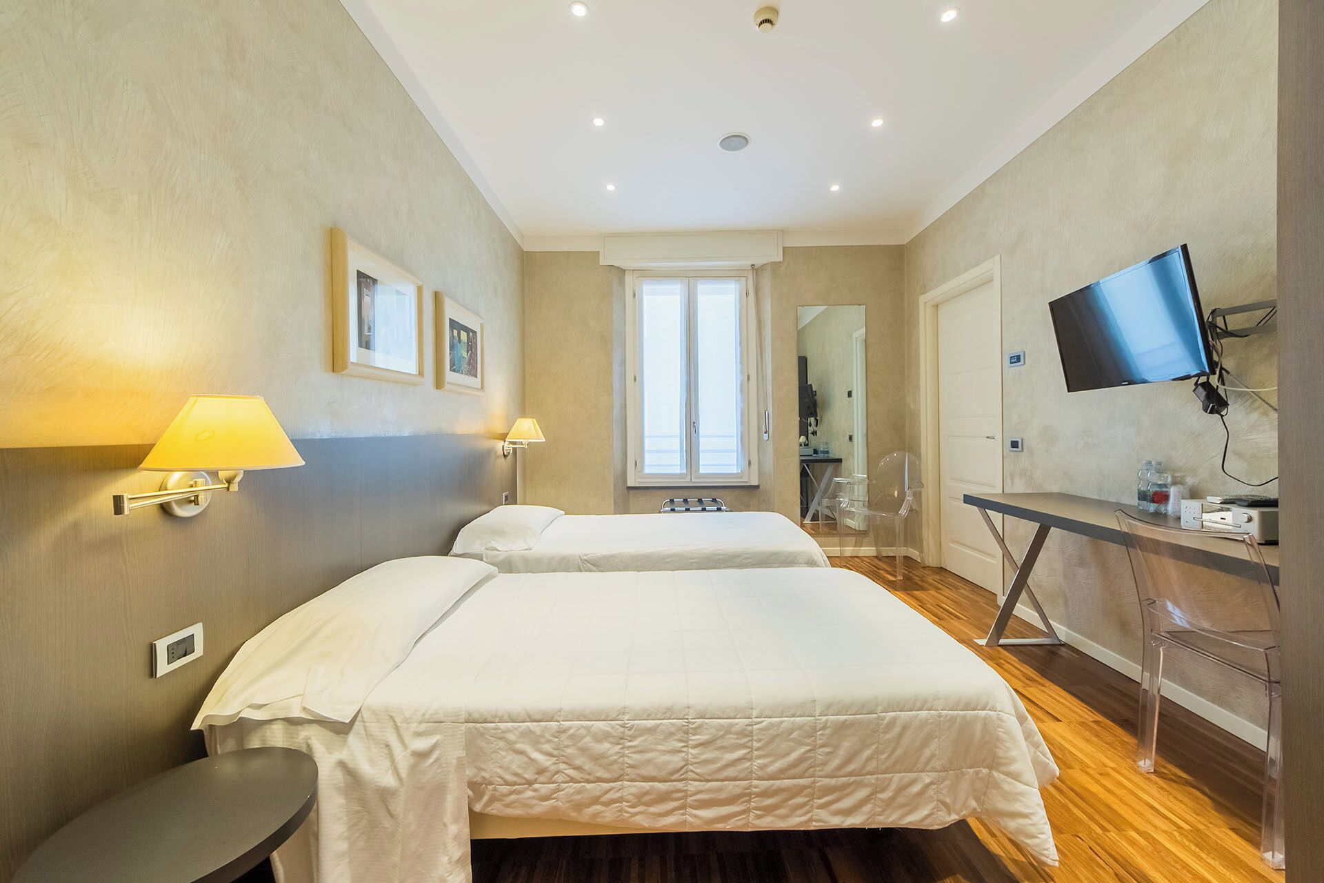 Ein Hotelzimmer mit zwei Betten, einem Schreibtisch mit Computer, einem Fernseher und einem durch eine Tür einsehbaren Badezimmer.