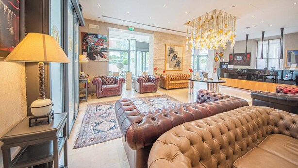 A spacious lobby with leather sofas, a patterned rug, and a modern chandelier. - Century Hotel (Parma)
