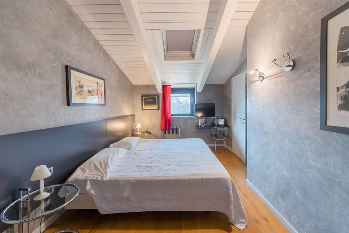 A bedroom with a bed, bedside table, lamp, and a window with a red curtain.