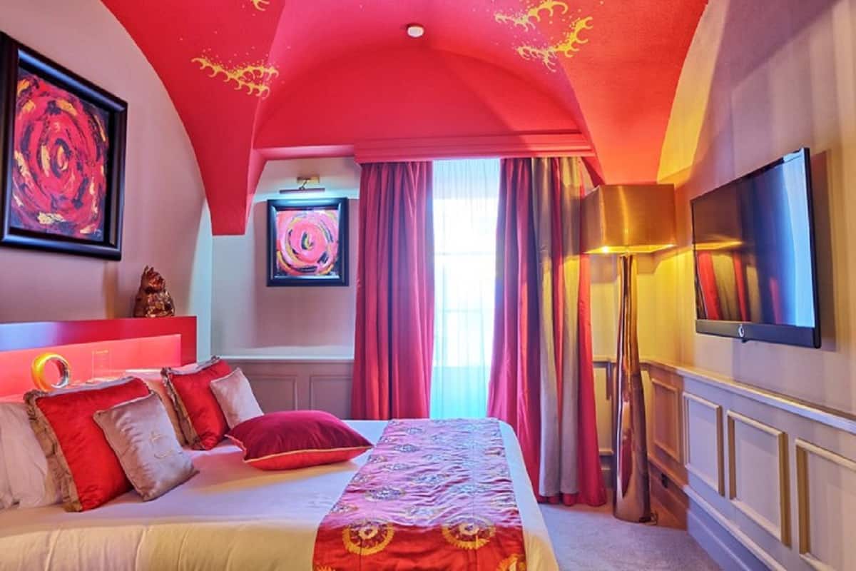 A bedroom with a large bed, red and white bedding, a ceiling with a red arch, and a flat-screen TV mounted on the wall.