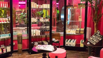 A retail space with shelves stocked with various products, a small seating area, and a large potted plant.