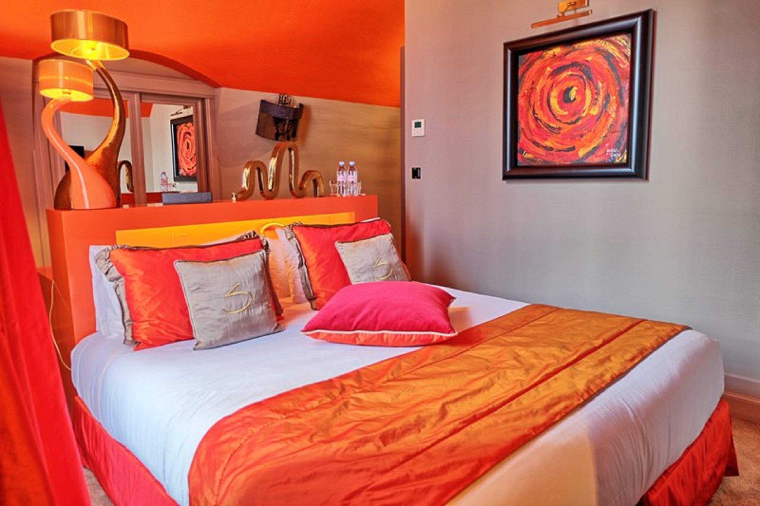Ein Hotelzimmer mit einem großen Bett, orangefarbener Bettwäsche, einem Spiegel und einem Bild an der Wand.