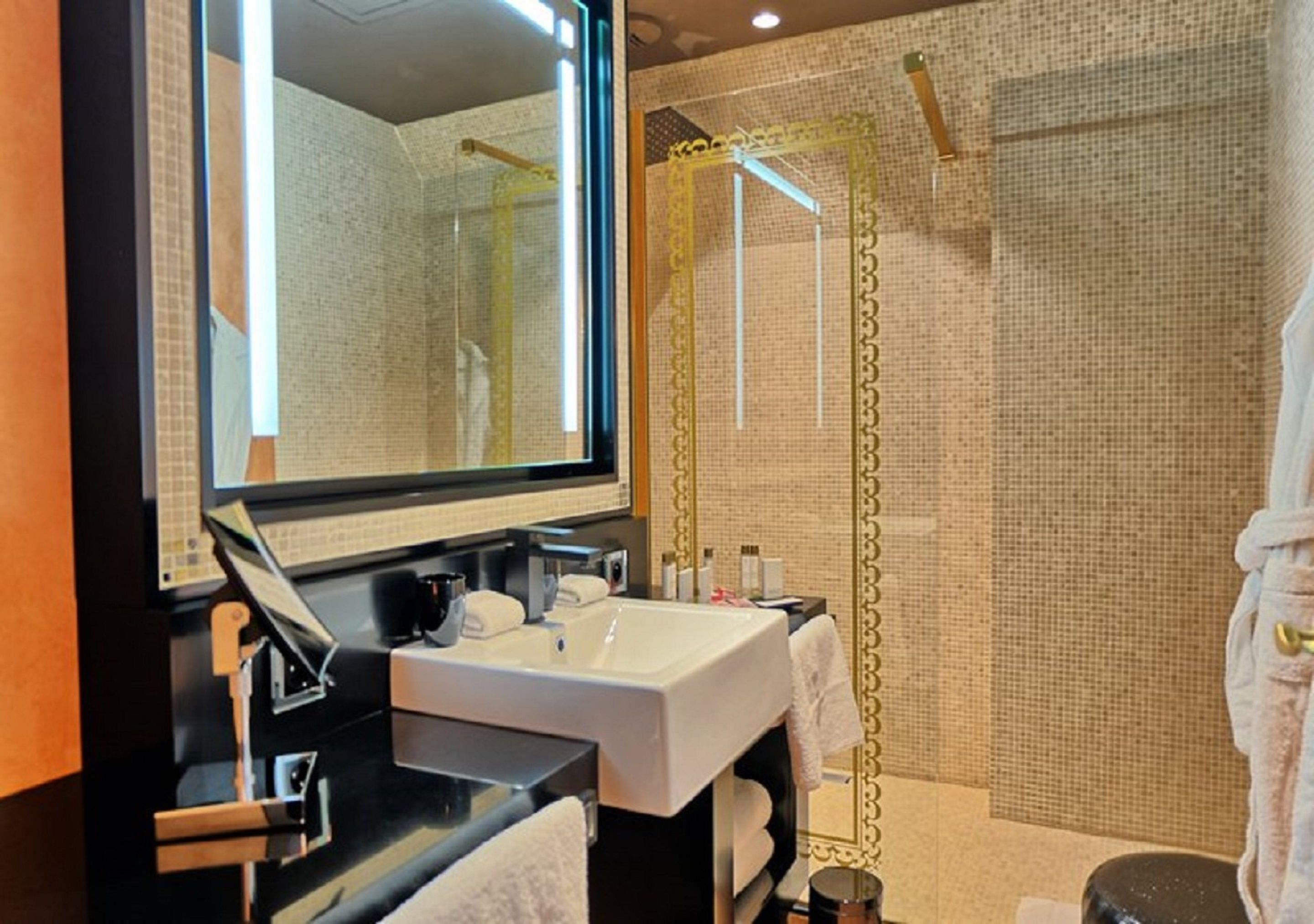 Un baño moderno con un espejo grande, un lavamanos blanco y una zona de ducha con cortina dorada.