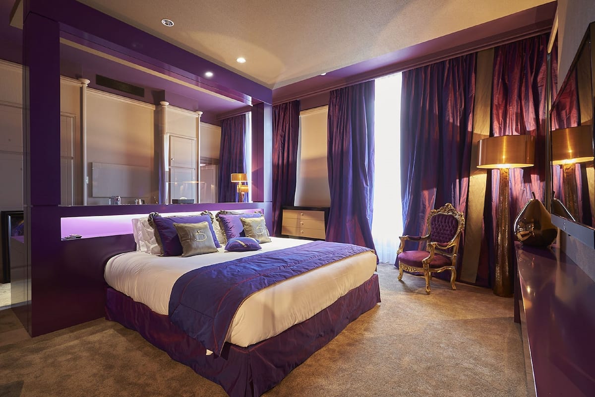 A modern bedroom with a large bed, a vanity with a mirror, and a chair.