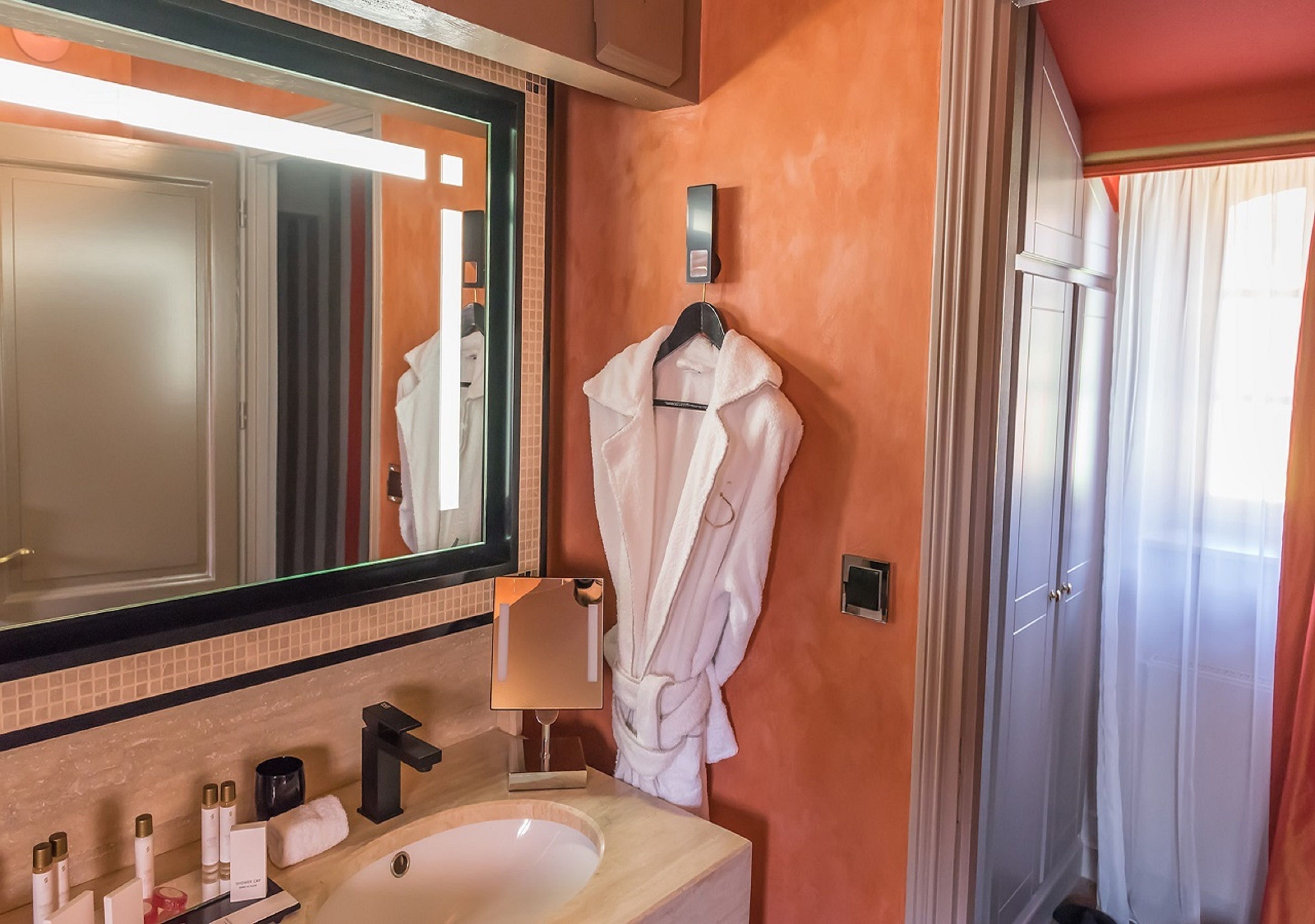 A bathroom with a large mirror, a sink, a robe hanging on the wall, and a shower area.
