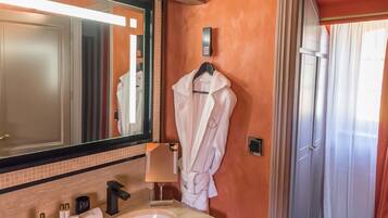 Une salle de bain avec un grand miroir, un lavabo, un peignoir accroché au mur et un espace douche.