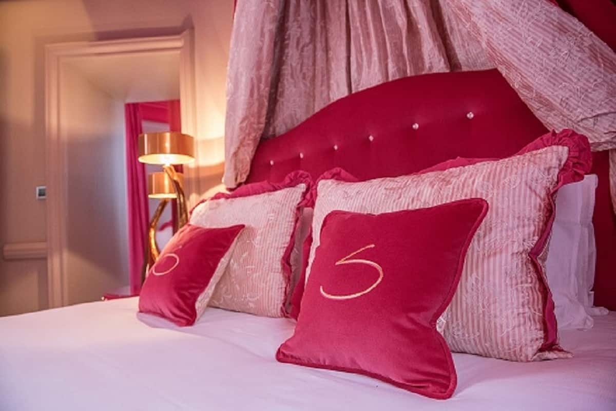 A bed with a red headboard, two pillows with a number '5' on them, and a lamp in the background.