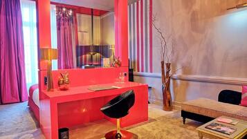 A room with a red vanity, a black chair, a small table with magazines, and a decorative vase.
