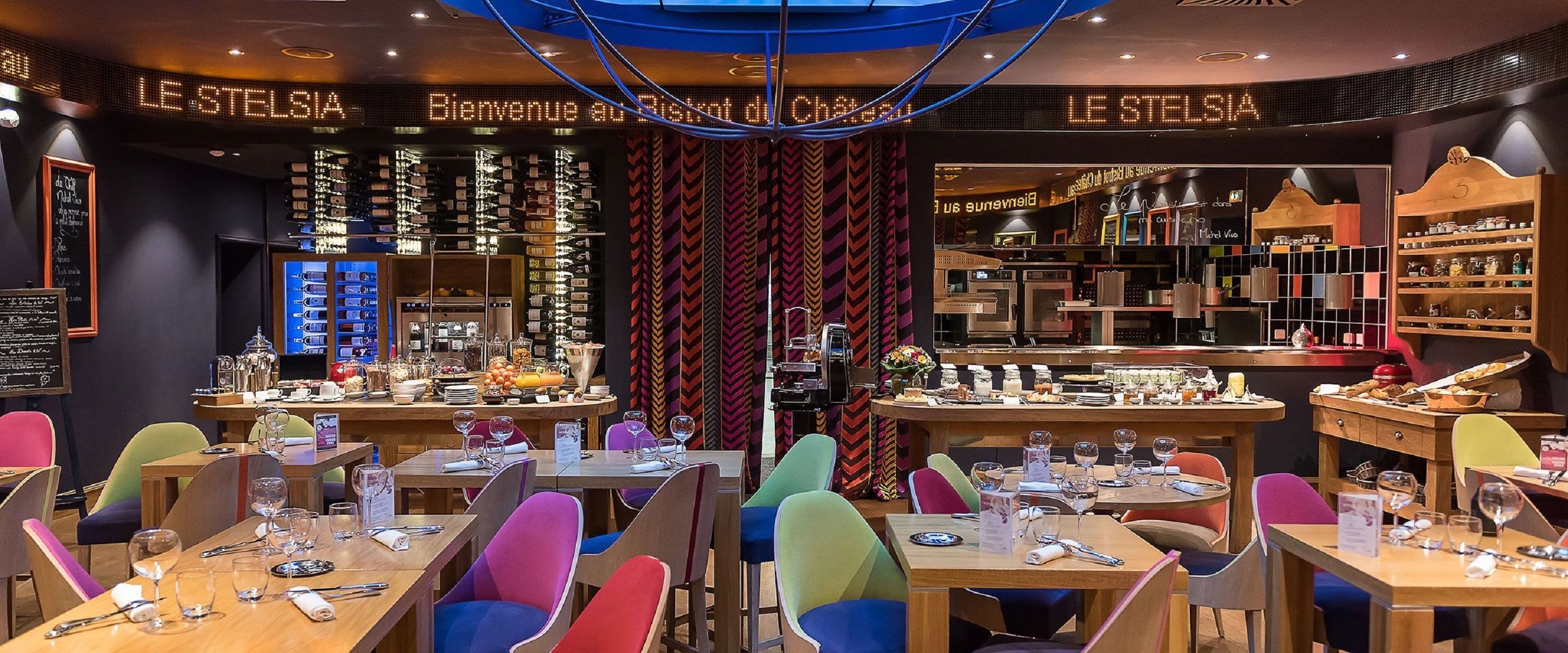 Un restaurant avec des chaises aux couleurs vives, une variété de plats exposés et une enseigne sur laquelle on peut lire « LE STELSI ».