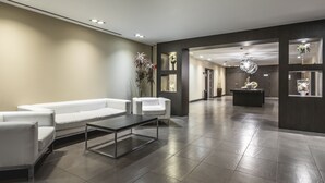 A modern lobby with a reception desk, seating area, and decorative plants.