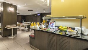 A breakfast buffet area with various food items and a television screen in the background.