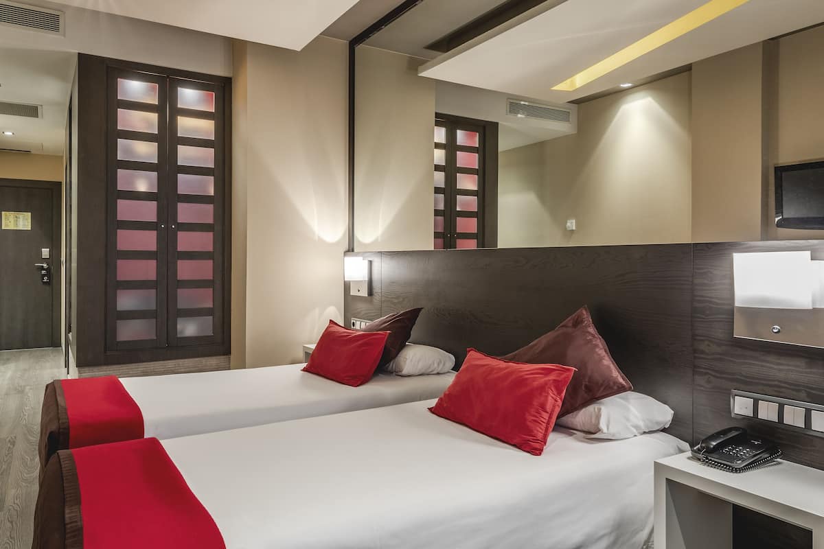 A hotel room with two beds, a large mirror, a TV, and a bedside table with a phone.