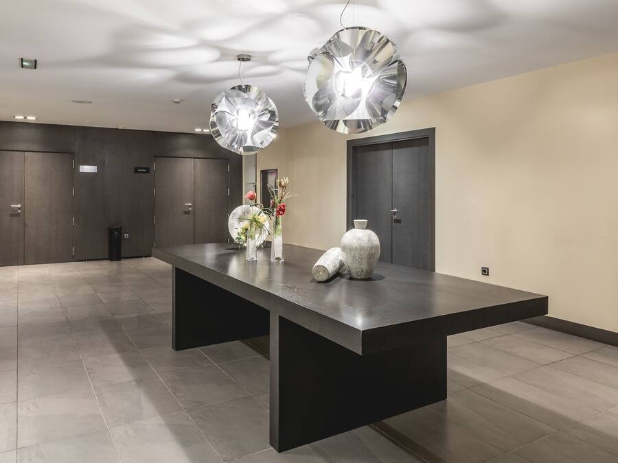 Un área de recepción moderna con un mostrador alargado, dos grandes lámparas colgantes decorativas y un jarrón con flores.