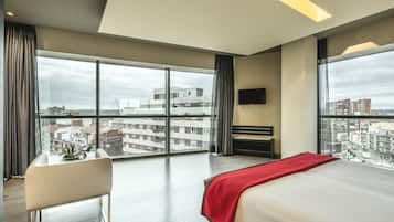 Habitació d'hotel moderna amb una finestra gran, un llit, un escriptori i una televisió.