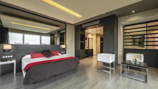 A modern hotel room with a large bed, bedside tables, a desk, and a seating area.