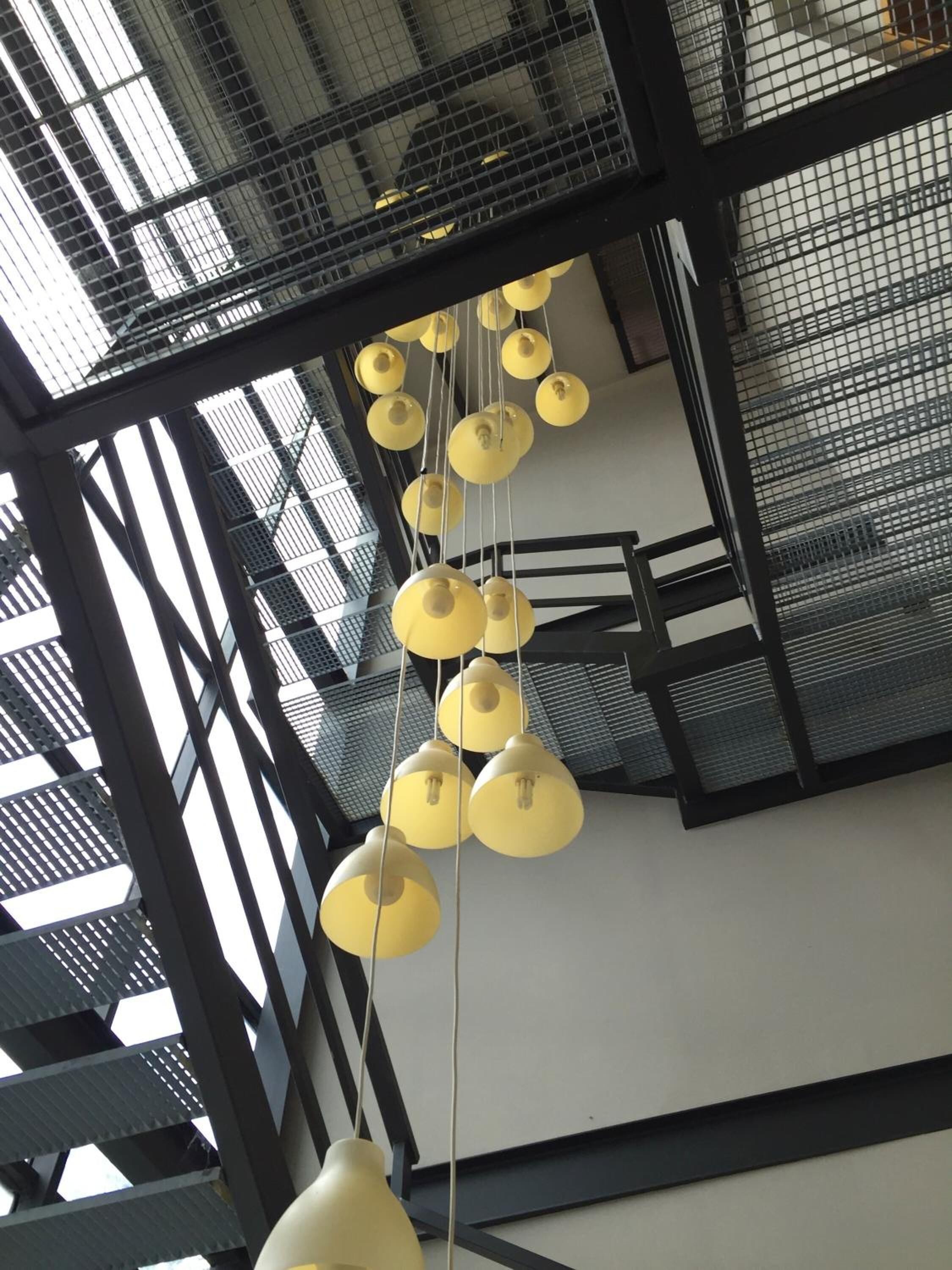 Un interior moderno con varios candelabros colgantes amarillos y una estructura de escaleras metálica.