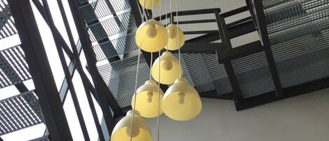 Un interior moderno con varios candelabros colgantes amarillos y una estructura de escaleras metálica.