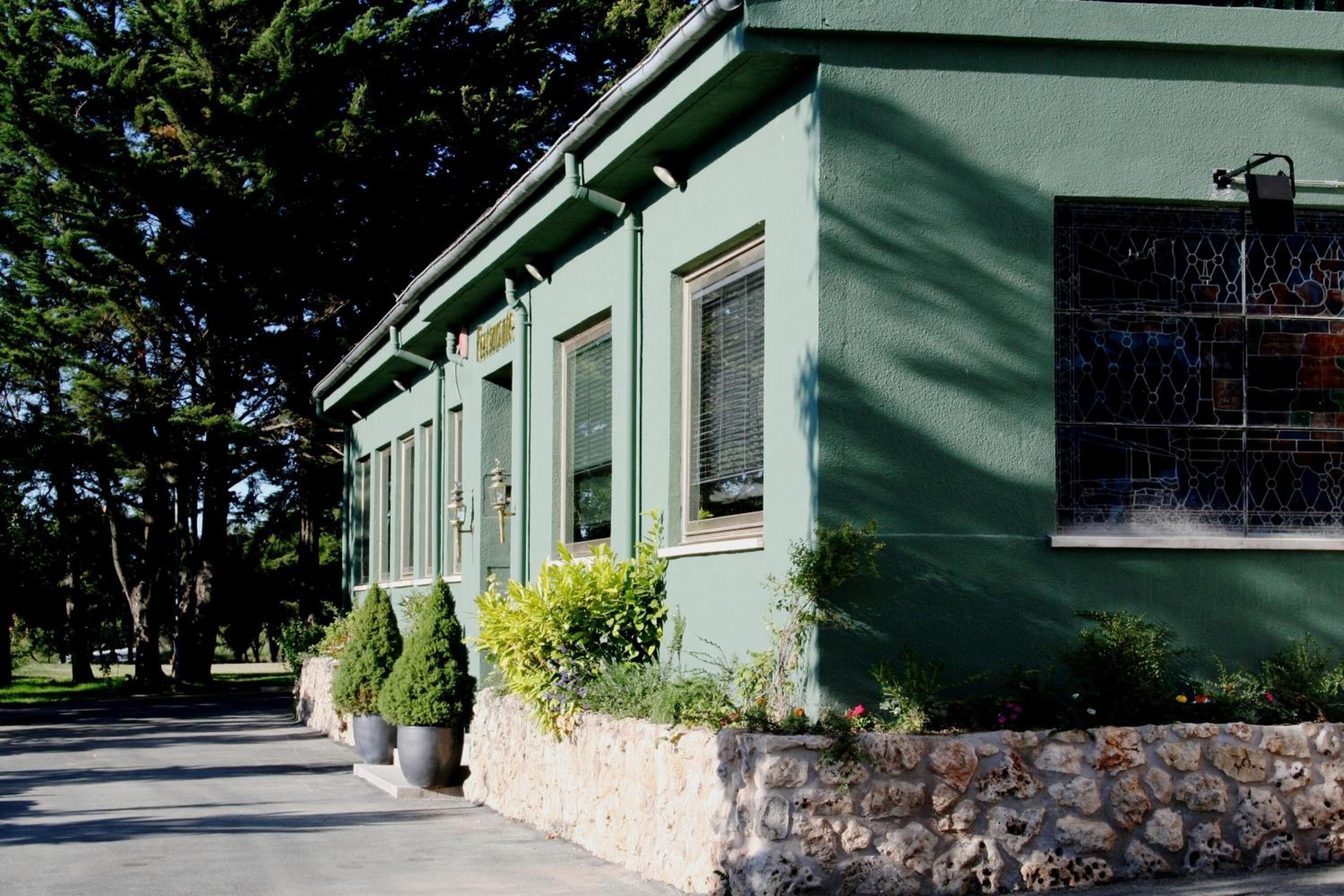 Un edificio con base de piedra y paredes exteriores verdes, con una hilera de ventanas y una puerta.
