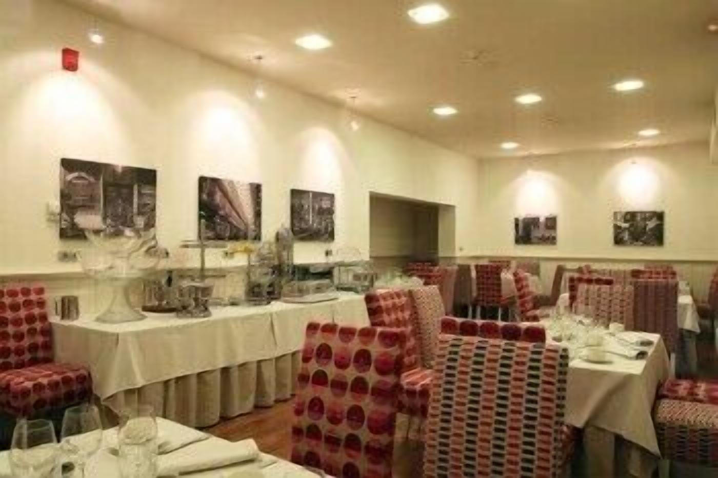 Un comedor con mesas dispuestas para el servicio, sillas con tapicería estampada y obras de arte colgadas en la pared.