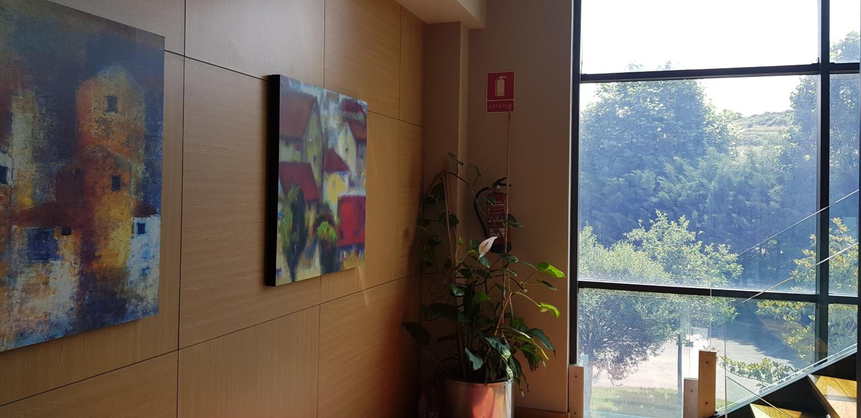 A room with wooden panel walls, two paintings, a potted plant, and a window with a view of trees.