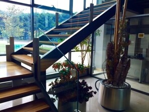 Una escalera moderna con barandillas de vidrio y escalones de madera, que conduce a una zona en el segundo piso con vistas al exterior.