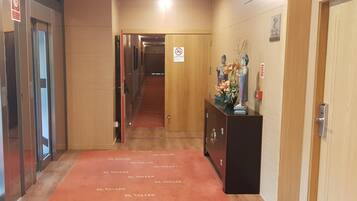 Corridoio di un hotel con ascensori, una porta di legno e una reception con un vaso di fiori.