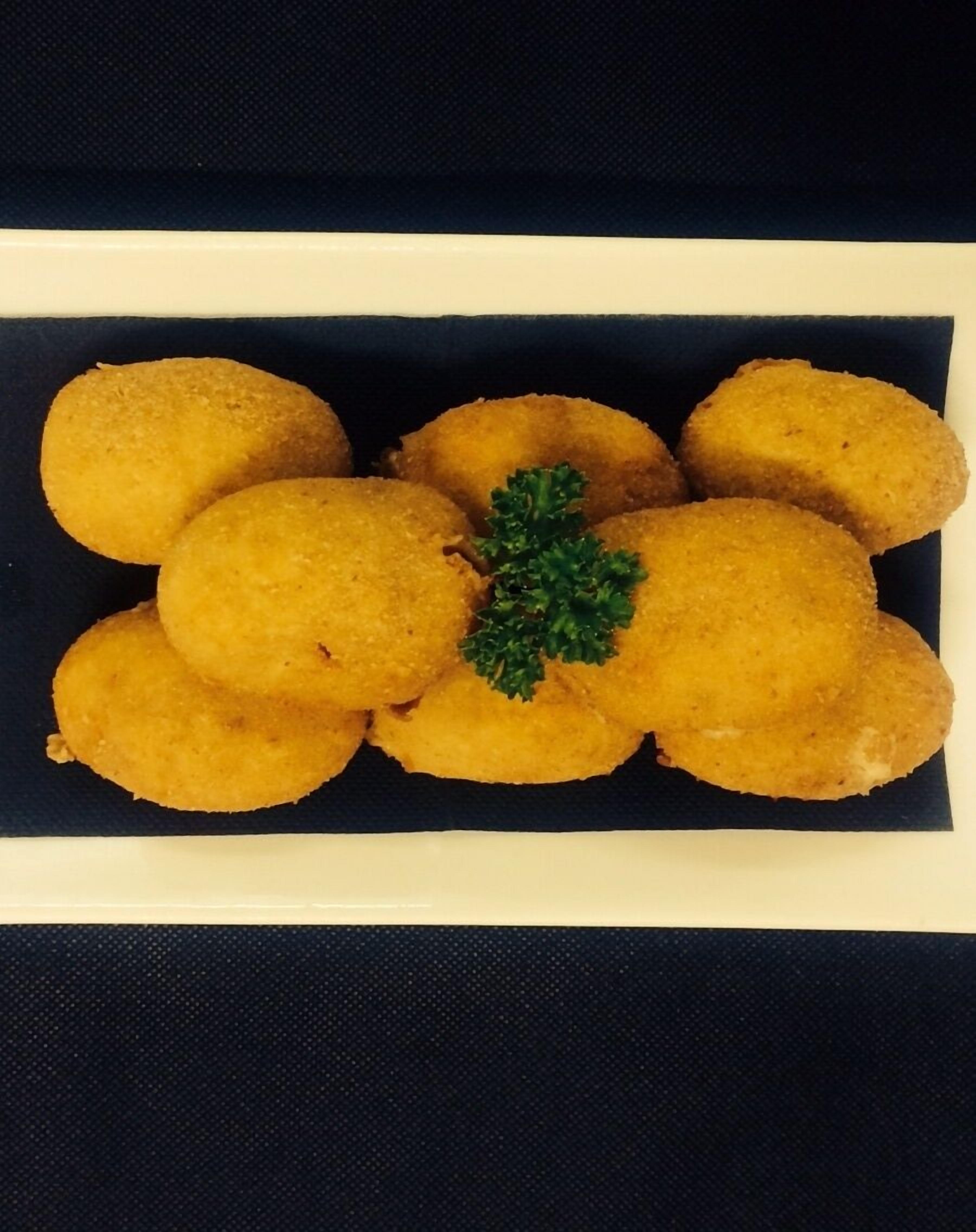 A rectangular white plate with golden-brown fried items, possibly croquettes, garnished with a sprig of parsley.