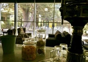 Una habitación con un ventanal grande, una mesa con frascos y una cafetera, y un sofá.