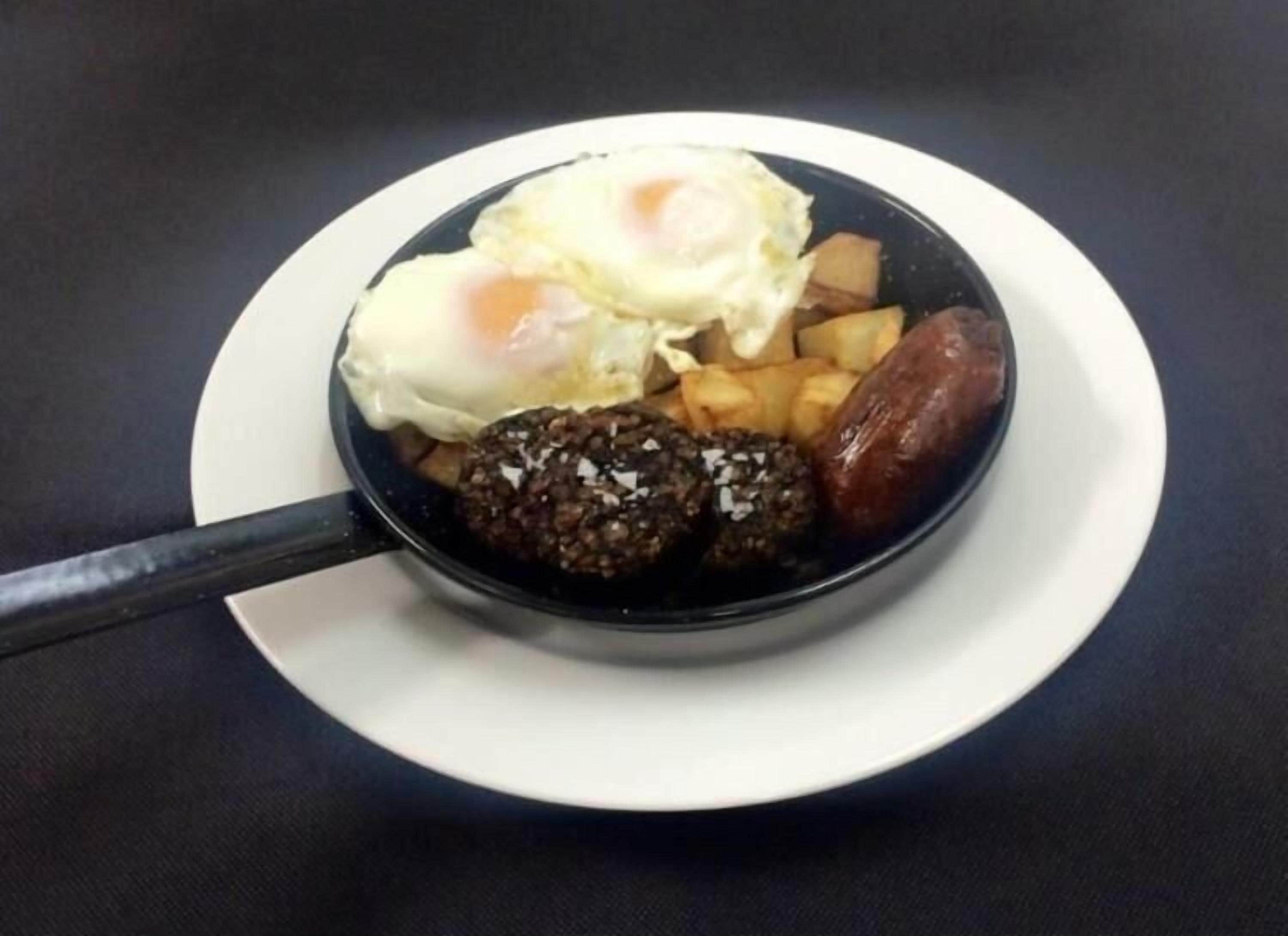 Una sartén negra con huevos, papas y salchichas sobre un plato blanco.