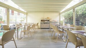 A spacious cafe with high tables and chairs, large windows, and a central counter with various items. - Hotel St. Moritz (Rome)