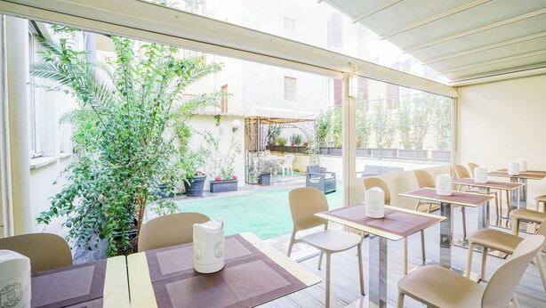 A restaurant with outdoor seating, tables with white tablecloths, and a view of a garden with potted plants. - Hotel St. Moritz (Rome)