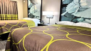 A hotel room with two beds, a nightstand, a lamp, and a large floral artwork on the wall.