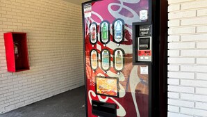 Een Coca-Cola automaat met een bord voor een spaarprogramma, naast een witte bakstenen muur.
