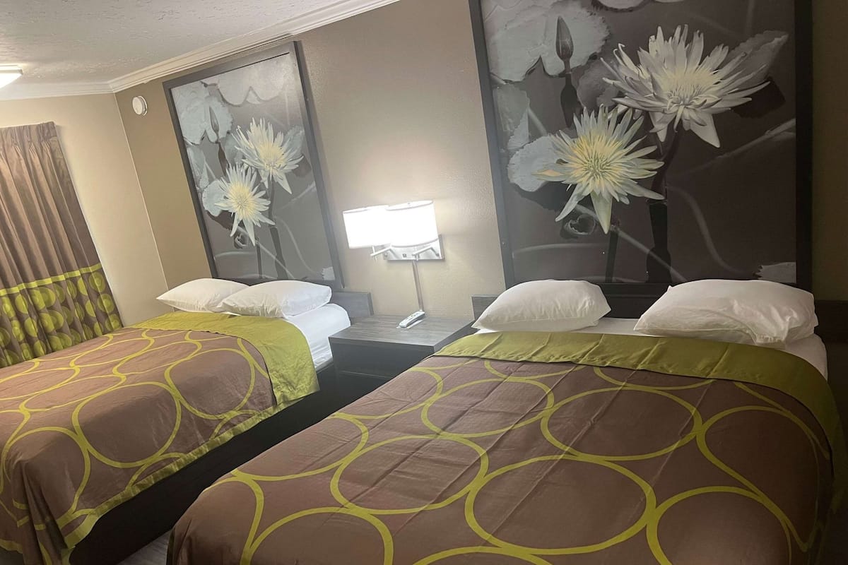Ein Hotelzimmer mit zwei Betten, einem Nachttisch mit Lampe und einem großen Blumenbild an der Wand.