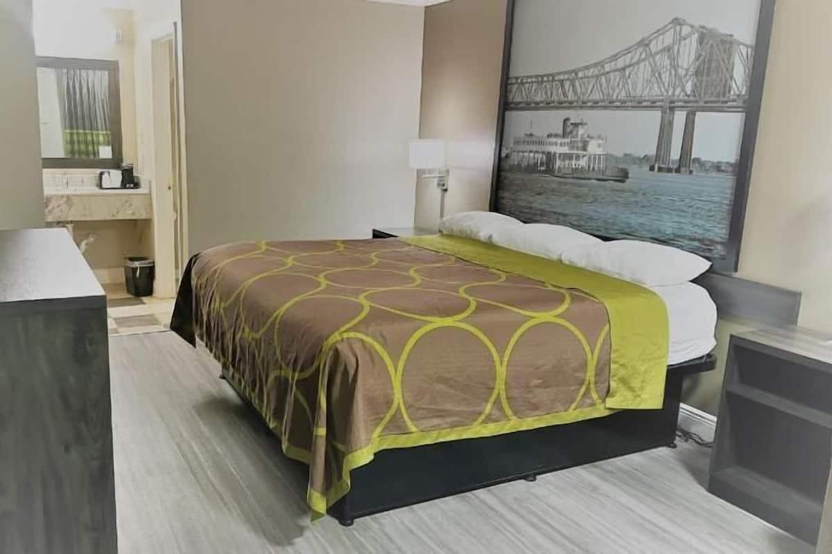 Ein Hotelzimmer mit Bett, Schreibtisch, Stuhl, Lampe, einem Bild einer Brücke und einem Badezimmer.