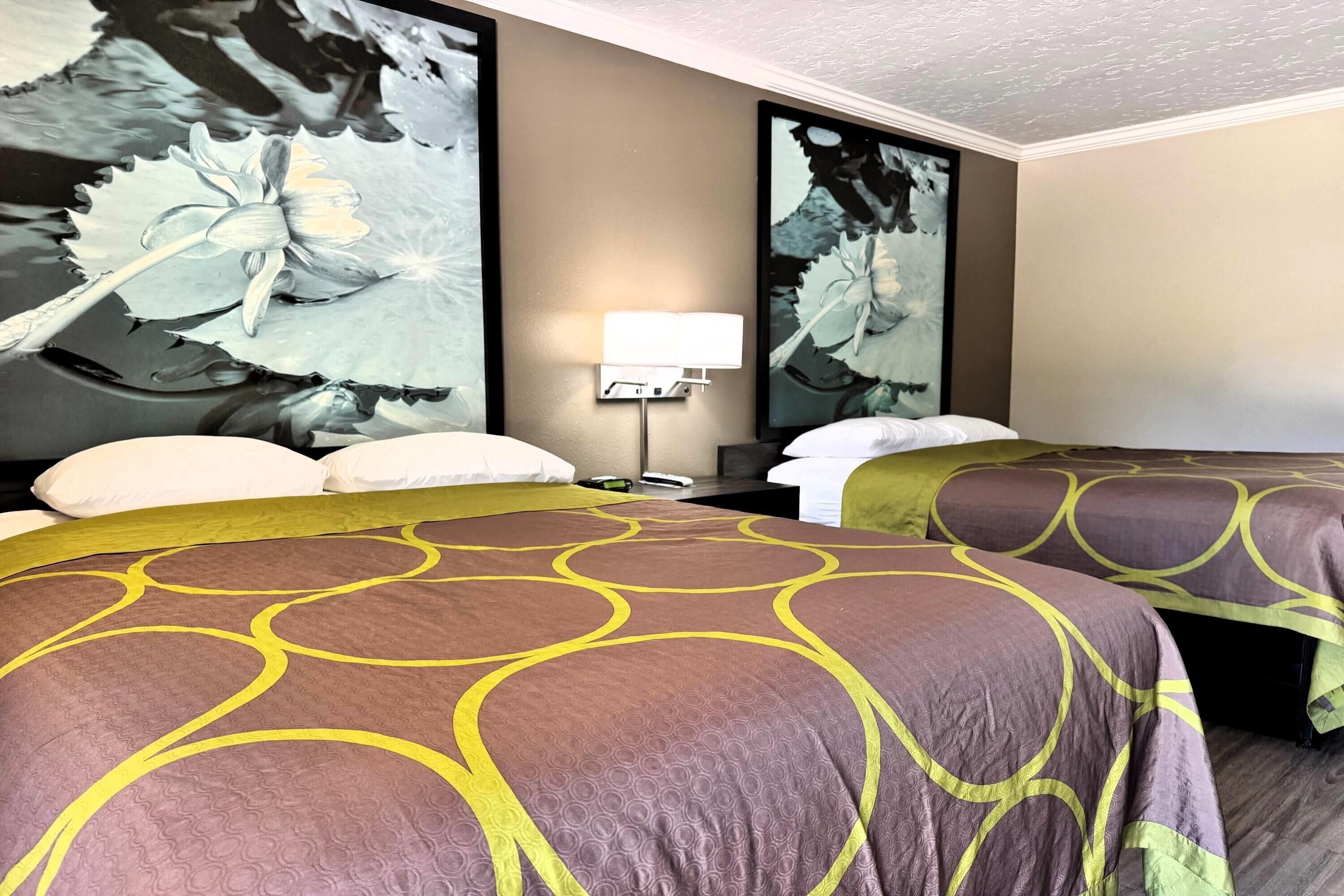 A hotel room with two beds, a nightstand with a lamp, and large floral artwork on the walls.