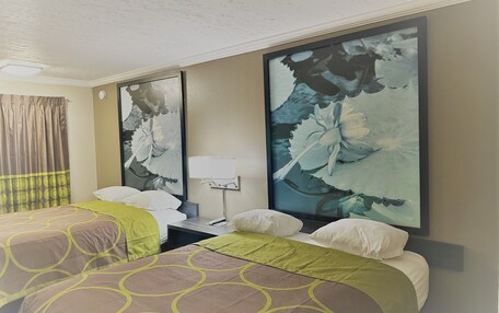 A hotel room with two beds, a nightstand, a lamp, and a large floral painting on the wall.