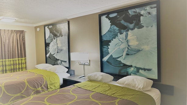 Een hotelkamer met twee bedden, een nachtkastje, een lamp en een groot bloemen schilderij aan de muur.
