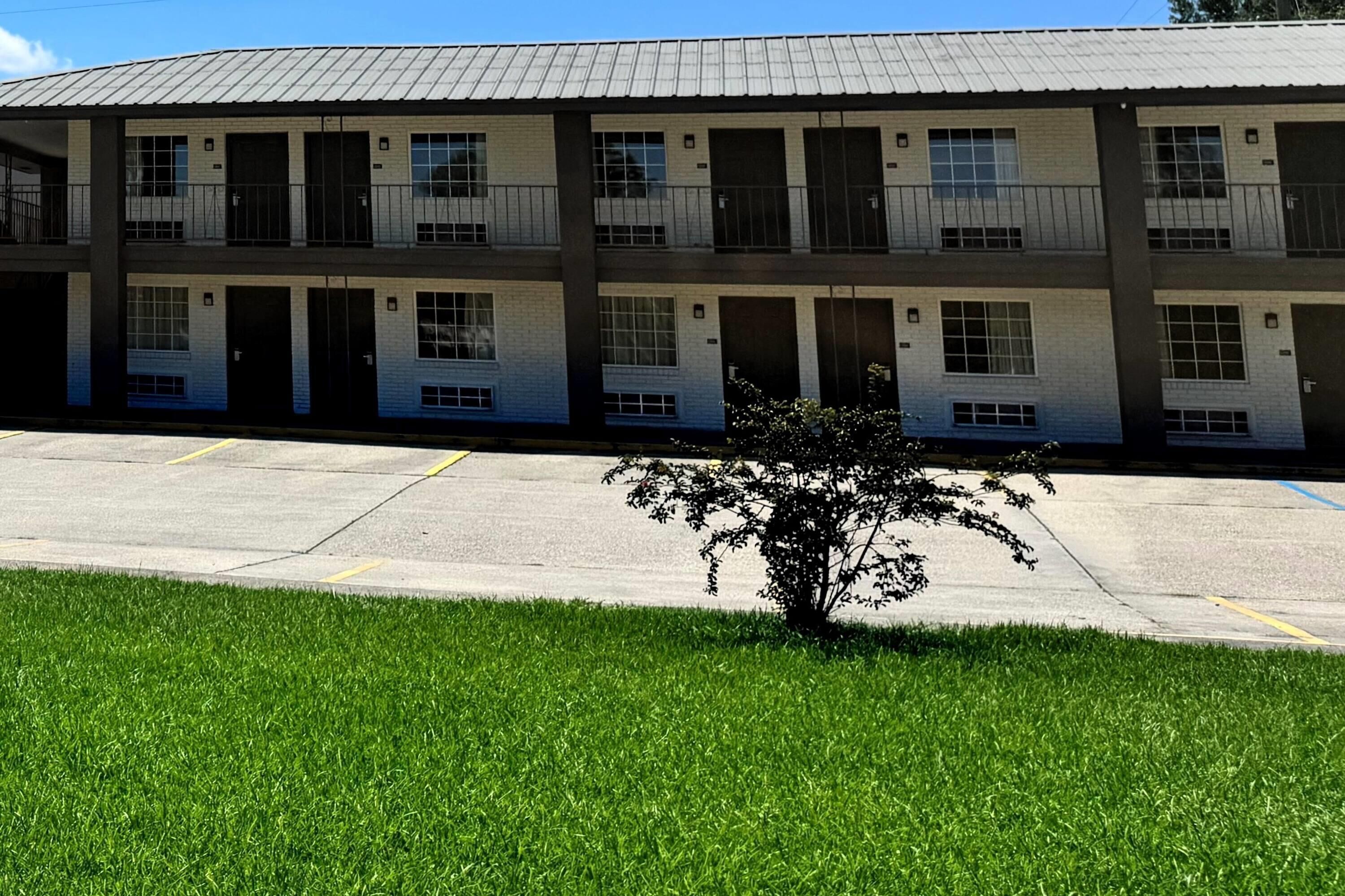 A multi-story motel with a flat roof, multiple balconies, and a parking lot in front.